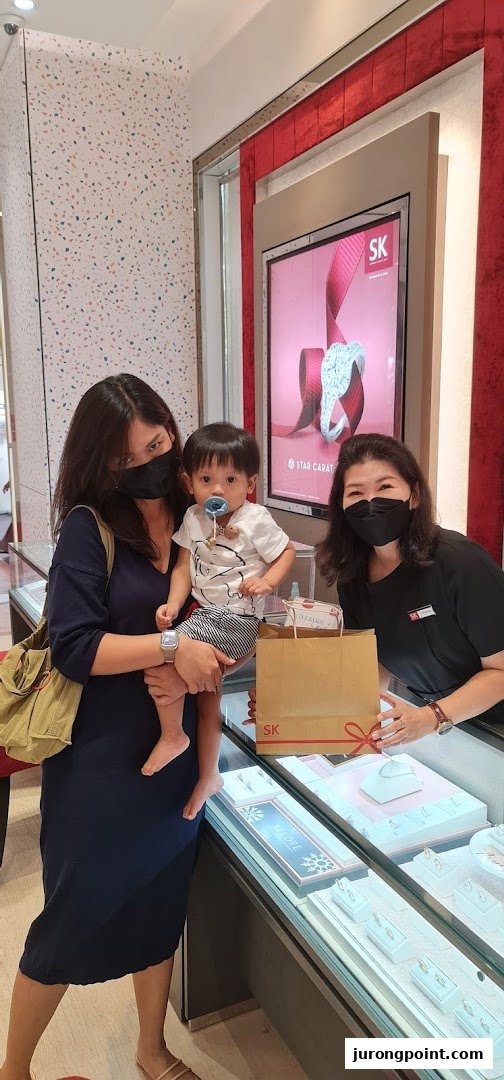 A customer with a baby and a staff member interact inside the SK Gold jewelry store.