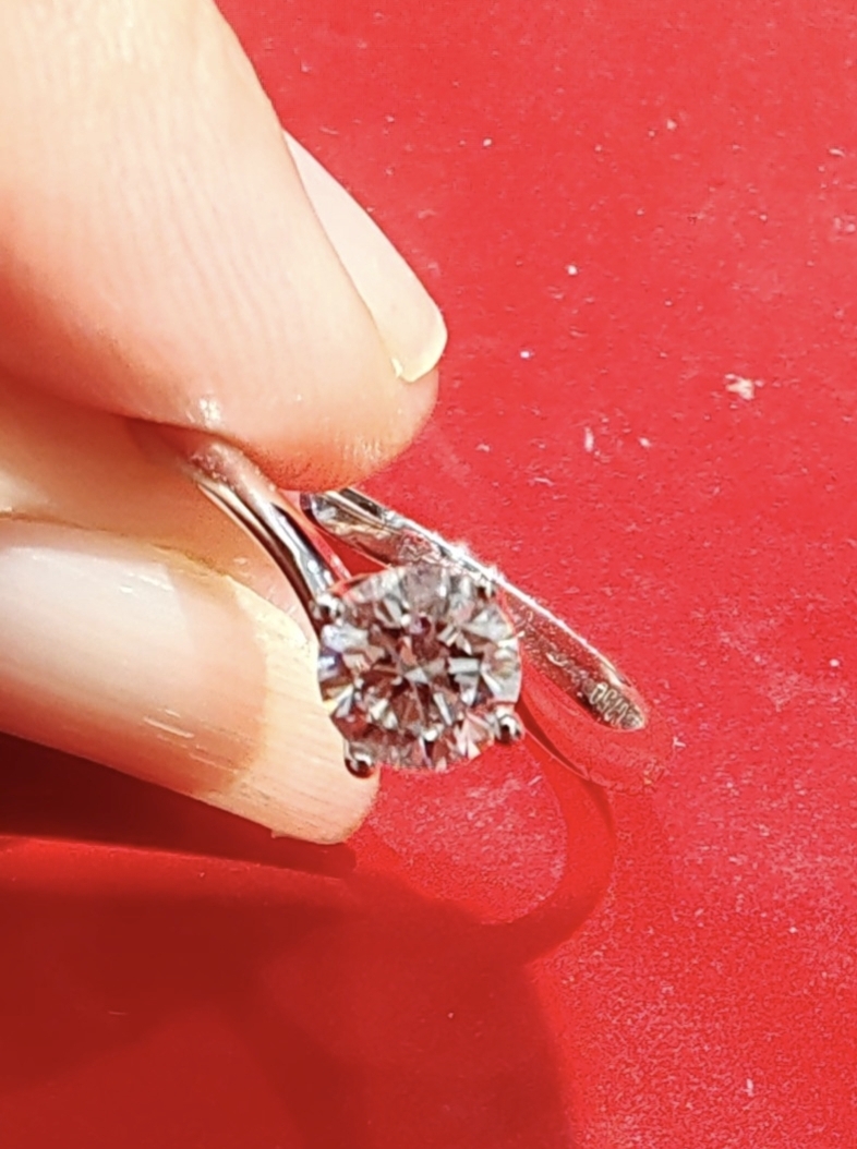 A hand holds a sparkling diamond ring against a vibrant red background.
