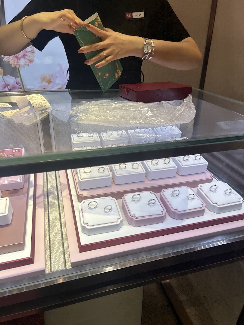A staff member at SK Gold prepares an item at a display counter filled with rings.
