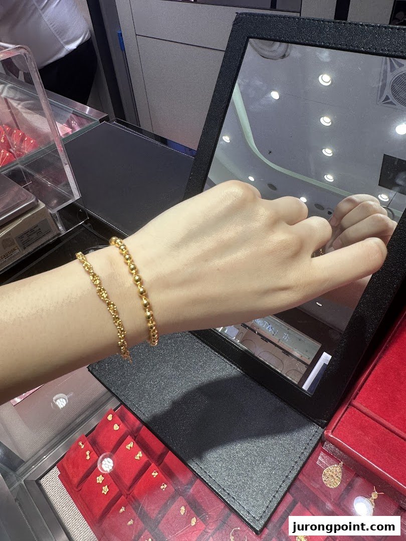A hand models two delicate gold bead bracelets in a jewelry store, reflected in a mirror.