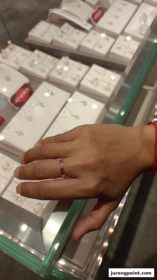 A hand wearing a ring, resting on a glass display case filled with various jewelry pieces.