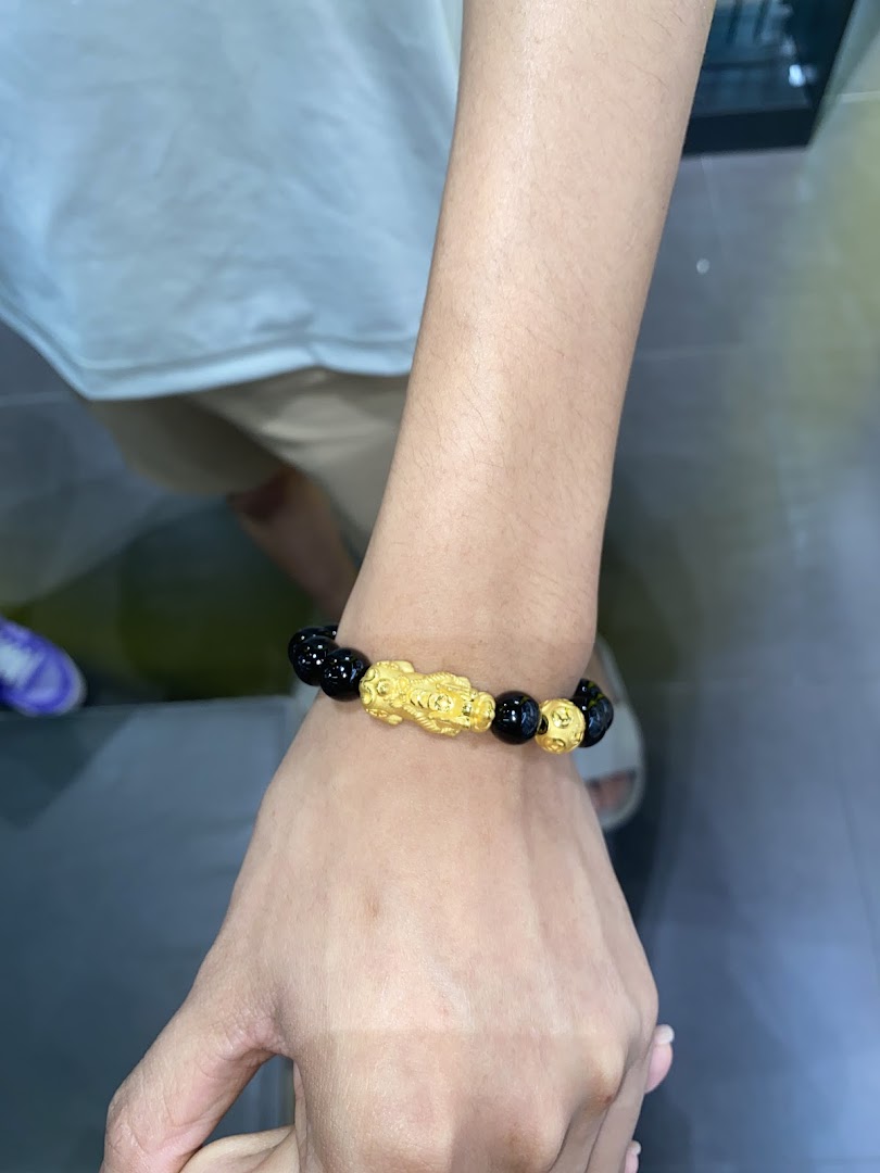 A person's arm showcasing a black and gold beaded bracelet with a mythical creature charm.
