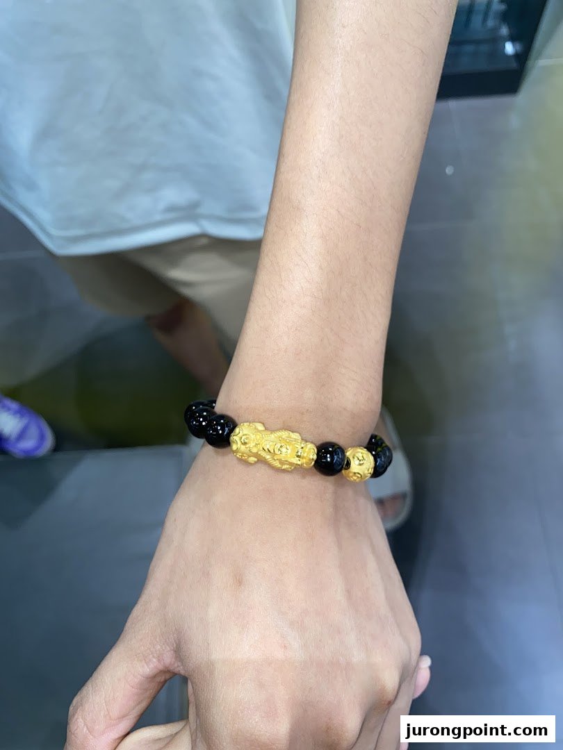 A person's arm showcasing a black and gold beaded bracelet with a mythical creature charm.