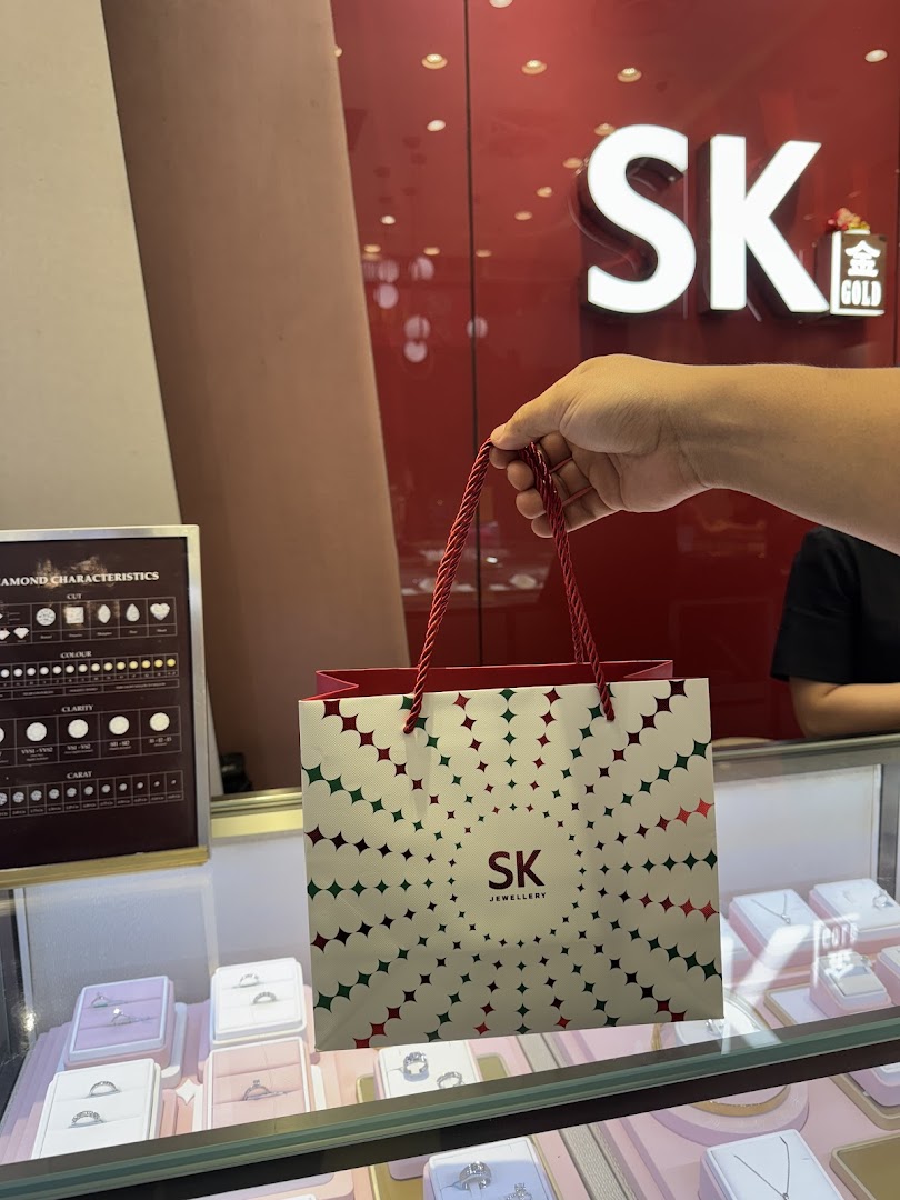 A hand holds an SK Jewellery shopping bag inside the SK Gold store, showcasing display cases.