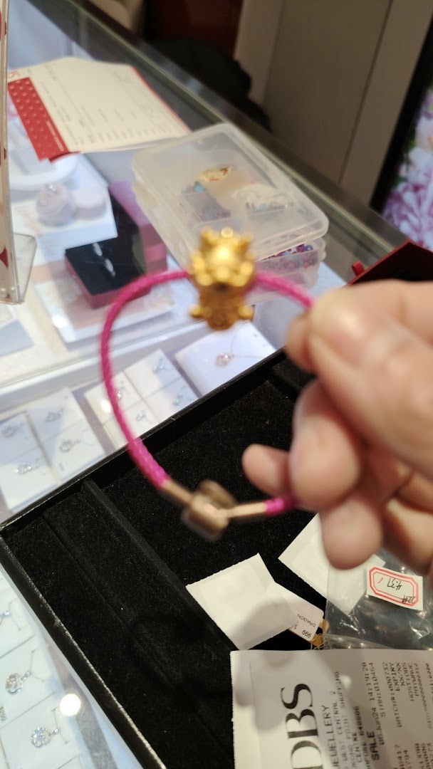 A hand holds a pink bracelet with a gold charm, displayed in a jewelry store.