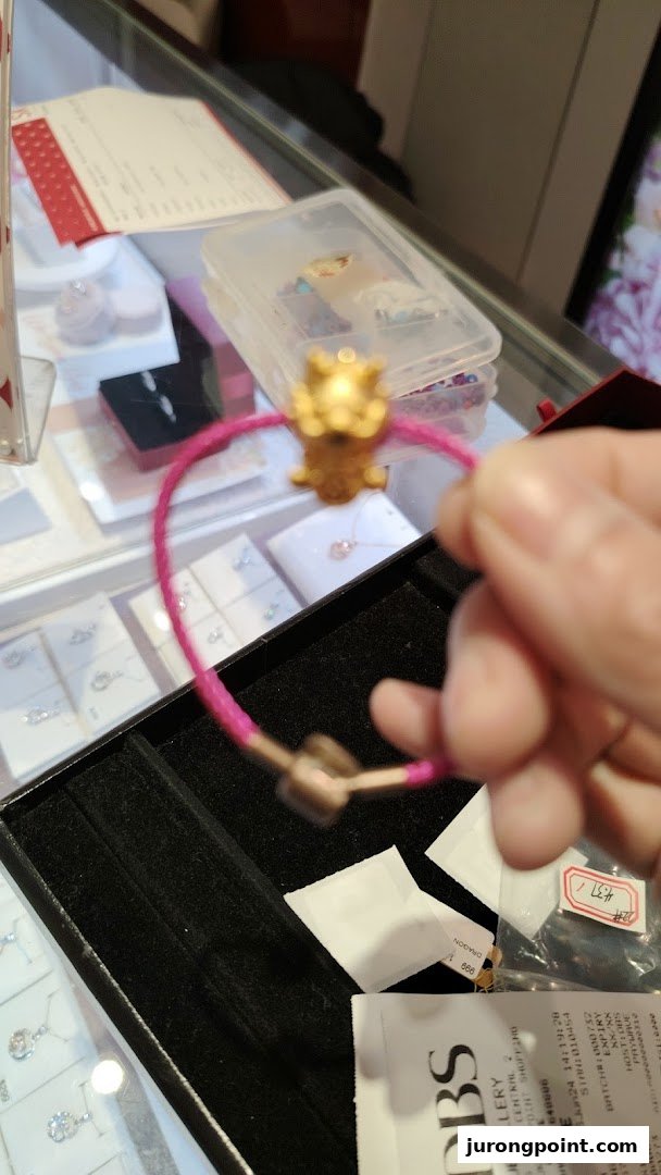 A hand holds a pink bracelet with a gold charm, displayed in a jewelry store.