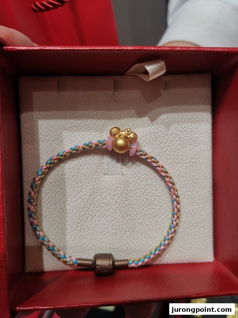 A colorful braided bracelet with a gold Mickey Mouse charm displayed in a red gift box.