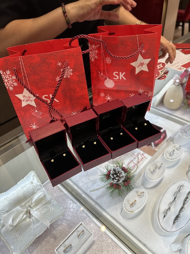Red SK Jewellery bags and open boxes with gold earrings on display, alongside other jewellery.