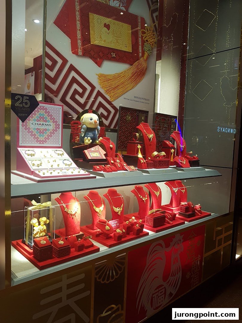 A vibrant SK Jewellery shop window display featuring gold jewellery, charms, and festive red decorations.