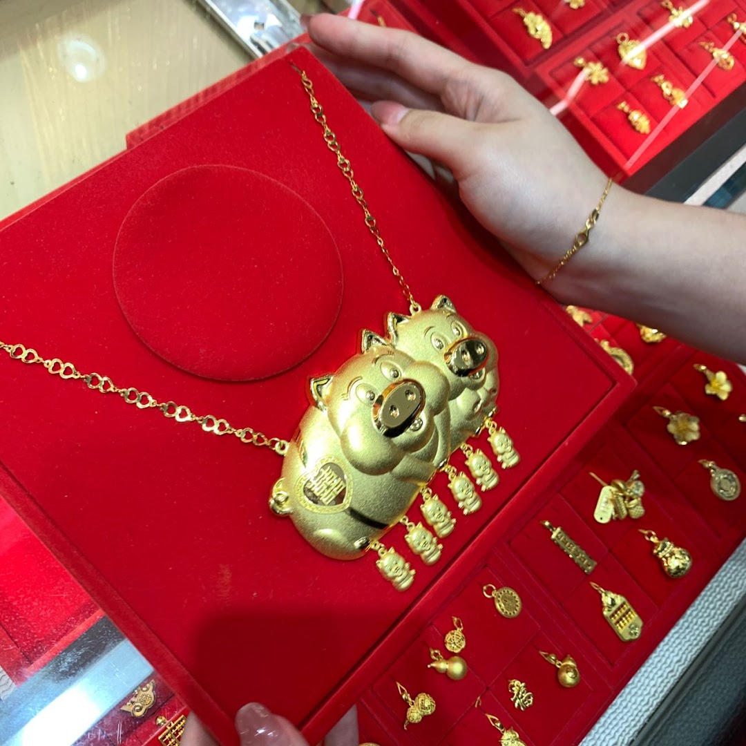 A close-up of a unique gold pig-themed necklace displayed on a red velvet tray, surrounded by other gold charms.