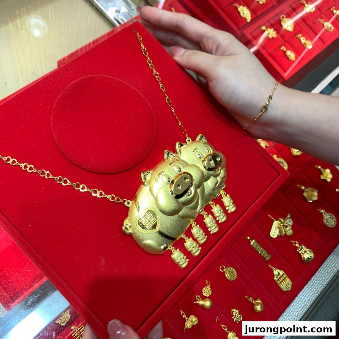 A close-up of a unique gold pig-themed necklace displayed on a red velvet tray, surrounded by other gold charms.
