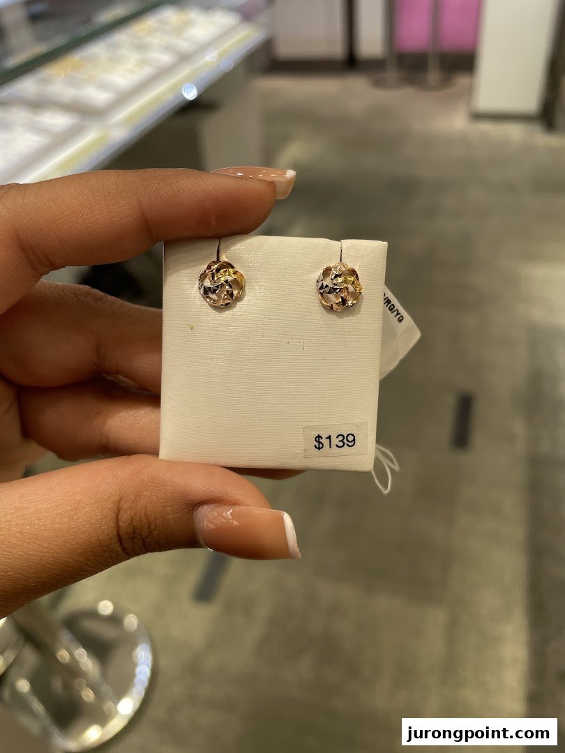A hand holds a pair of intricate gold earrings with a $139 price tag at SK Jewellery.