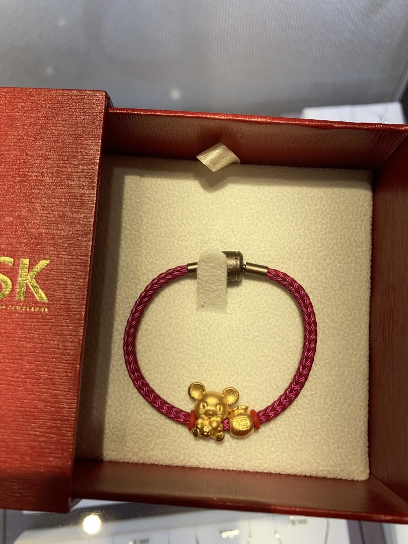 A gold rat charm bracelet with a red cord, presented in a red gift box.