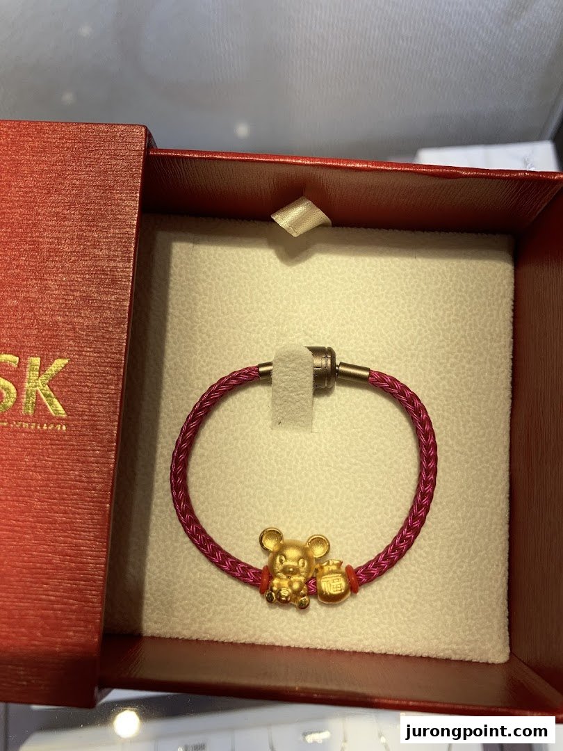 A gold rat charm bracelet with a red cord, presented in a red gift box.