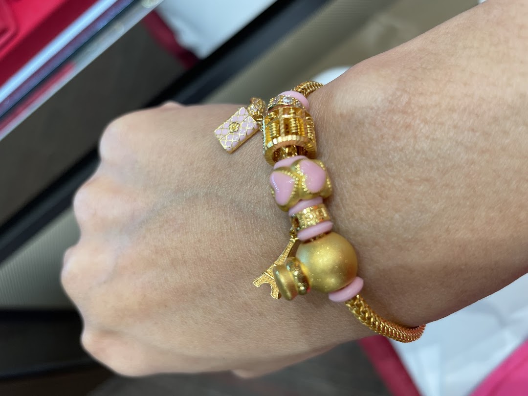 A close-up of a hand wearing a stylish gold bracelet adorned with pink enamel and charm beads.