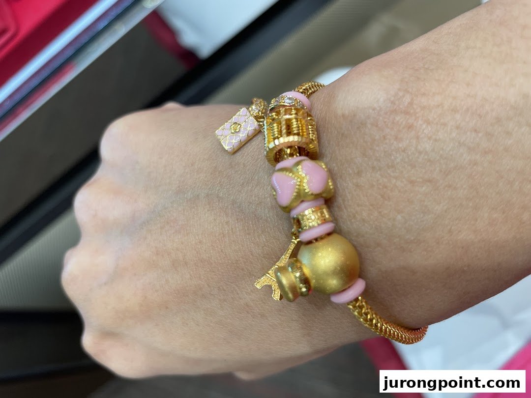 A close-up of a hand wearing a stylish gold bracelet adorned with pink enamel and charm beads.
