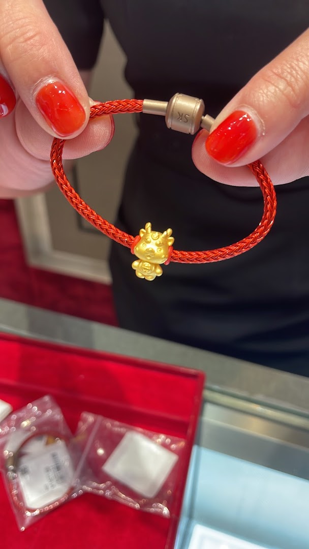 Close-up of hands holding a red braided bracelet with a golden ox charm.