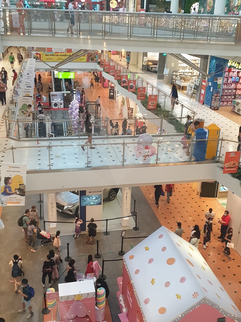 A vibrant multi-level shopping mall interior bustling with shoppers, various stores, and promotional displays.