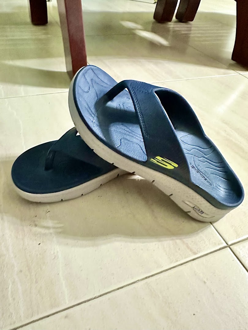 A pair of dark blue Skechers Arch Fit flip-flops with white soles on a tiled floor.
