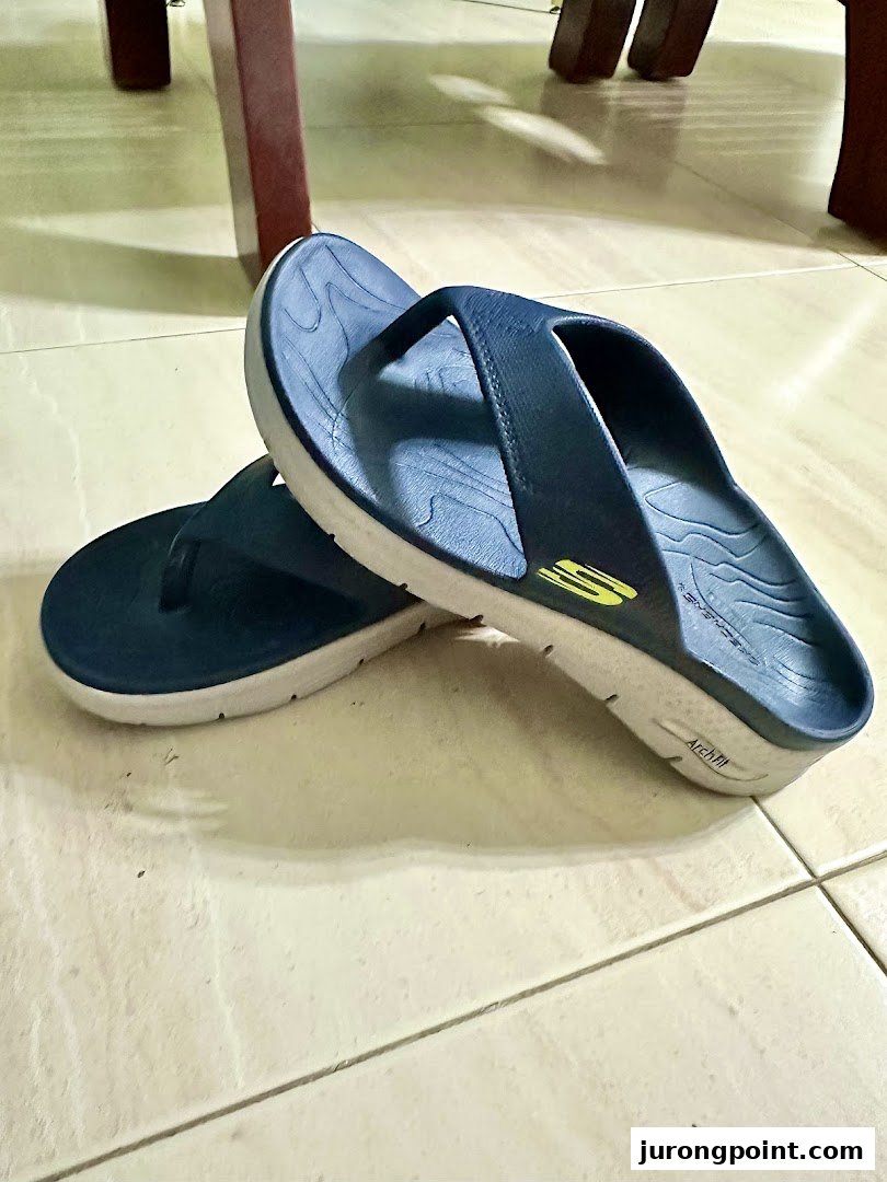 A pair of dark blue Skechers Arch Fit flip-flops with white soles on a tiled floor.