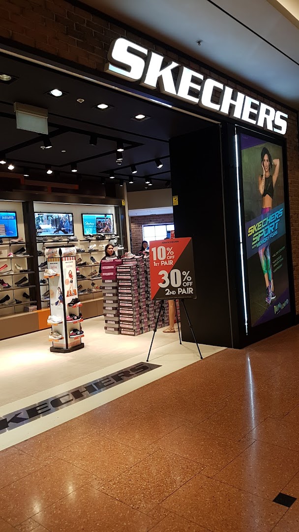 The entrance of a Skechers shoe store, featuring a prominent sale sign and interior view.
