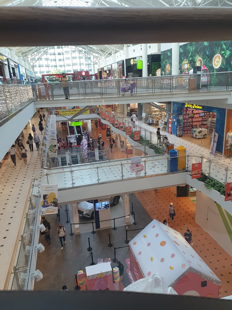 A multi-level shopping mall interior bustling with shoppers, featuring various retail stores and a car display.