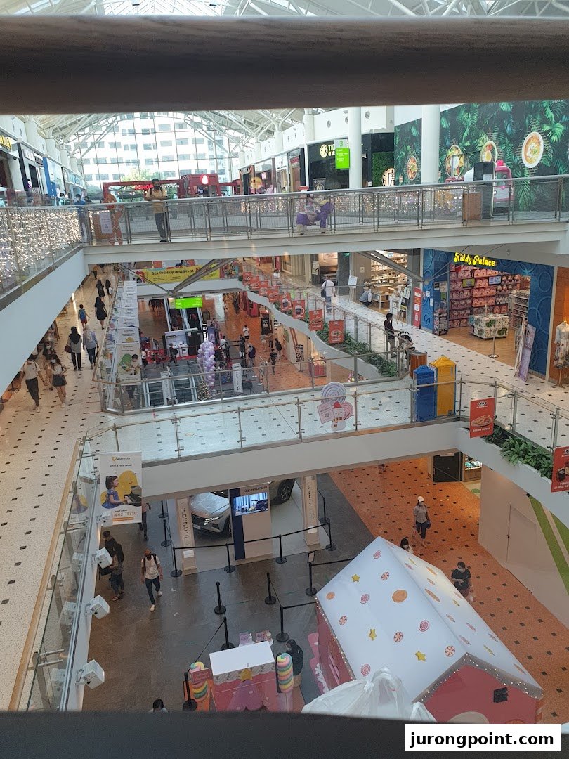 A multi-level shopping mall interior bustling with shoppers, featuring various retail stores and a car display.