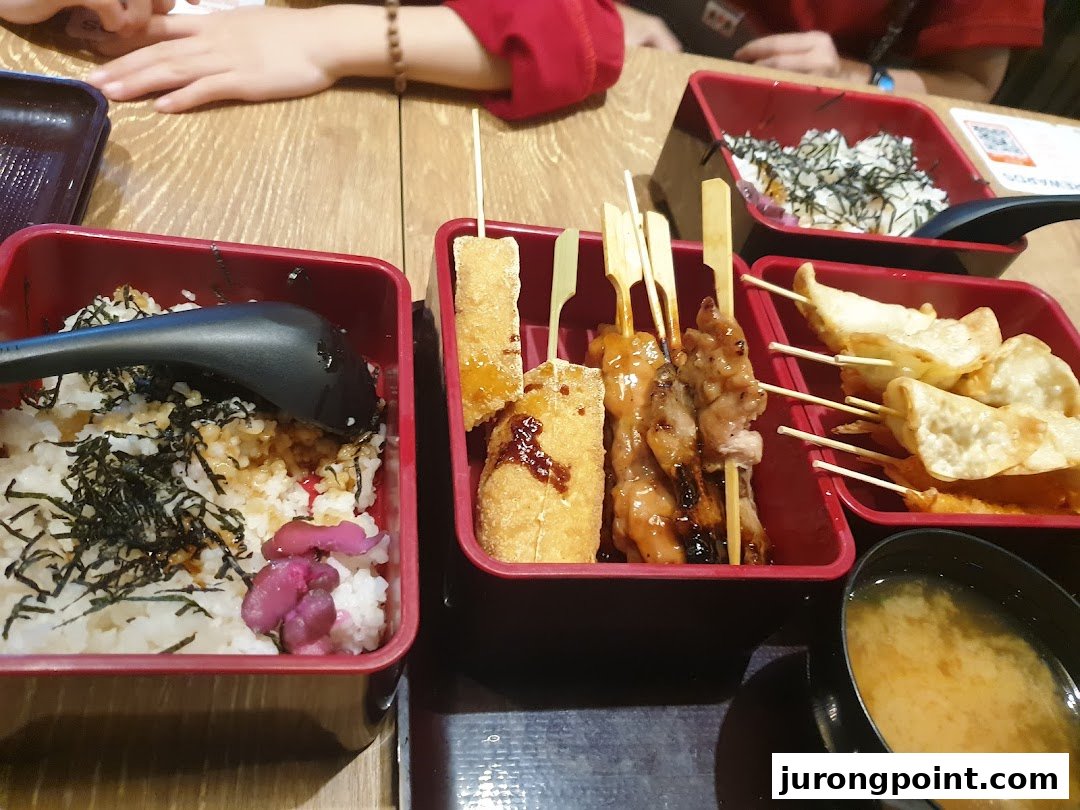 A close-up of various Japanese dishes, including rice bowls, skewers, dumplings, and miso soup.