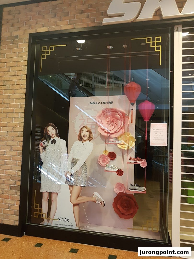 A vibrant Skechers shop window display featuring models, various shoe styles, and large floral decorations.