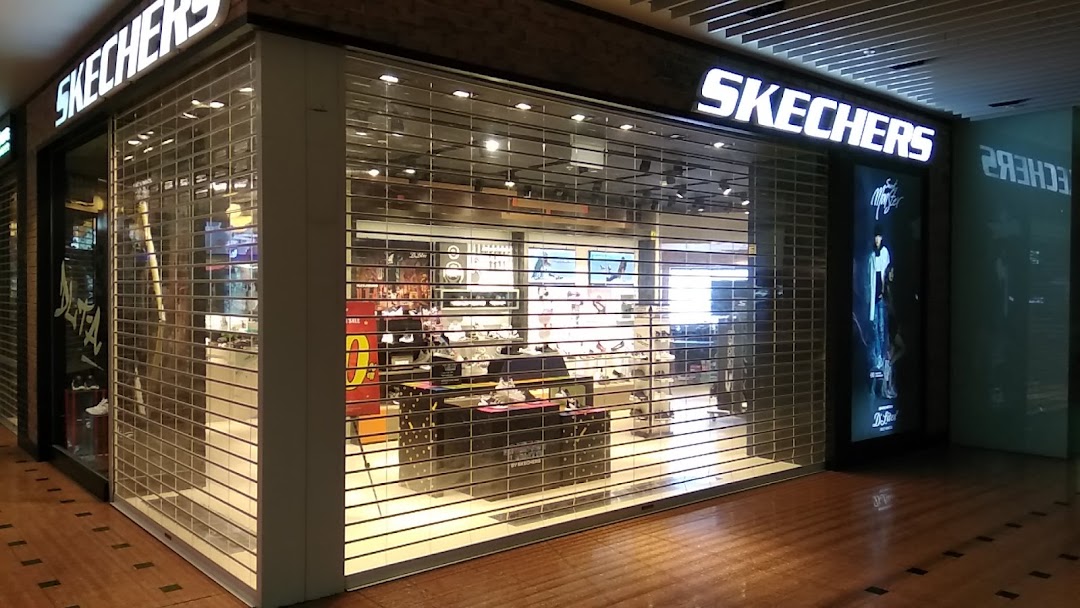 The Skechers retail store entrance, secured by a clear rolling gate, showcasing footwear displays inside.