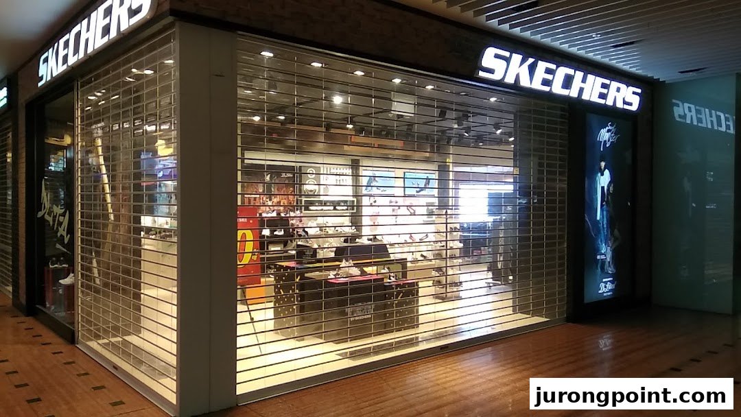The Skechers retail store entrance, secured by a clear rolling gate, showcasing footwear displays inside.