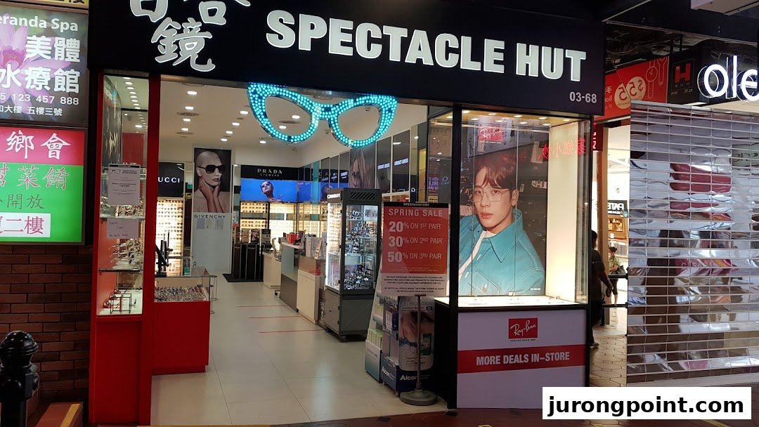 The storefront of Spectacle Hut, featuring a large glasses-shaped neon sign and promotional displays.