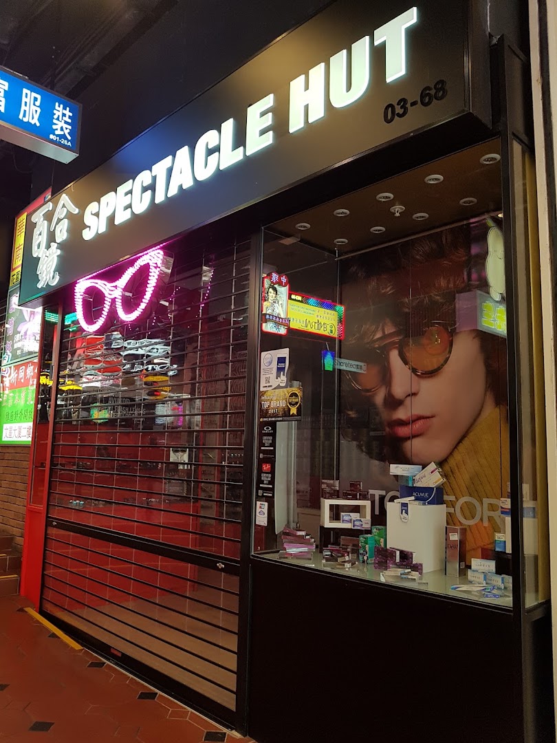 Illuminated storefront of Spectacle Hut, featuring a display window with eyewear and a closed security shutter.