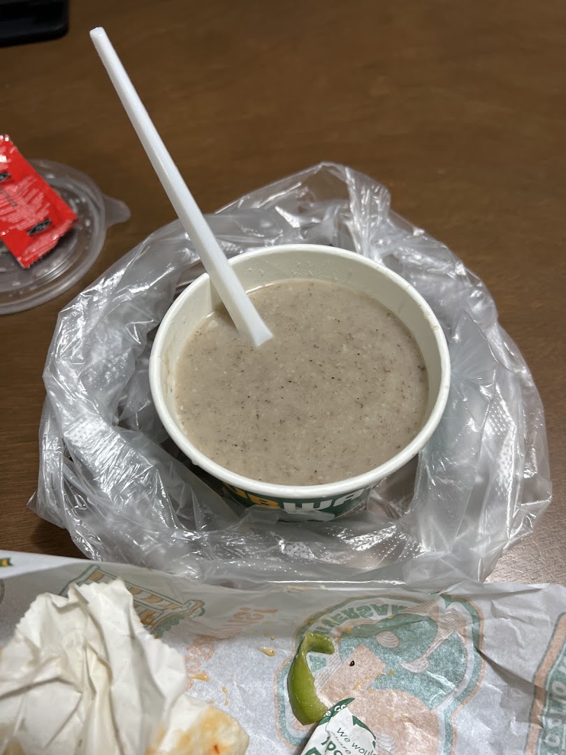 A cup of creamy mushroom soup from Subway, served with a spoon and plastic bag.