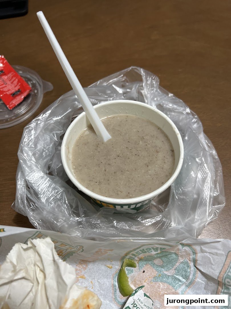 A cup of creamy mushroom soup from Subway, served with a spoon and plastic bag.