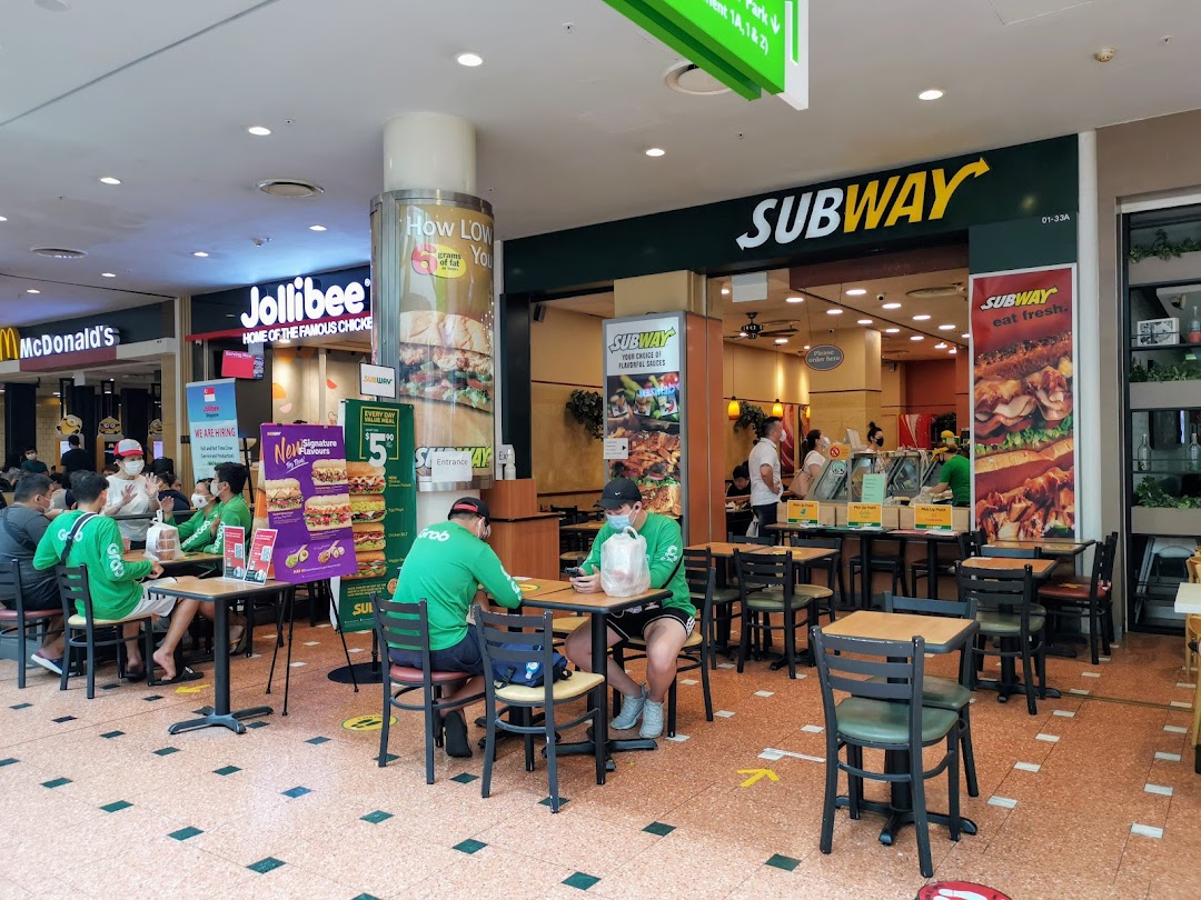 Subway shop interior with customers dining, showing its entrance and adjacent fast-food restaurants in a mall.
