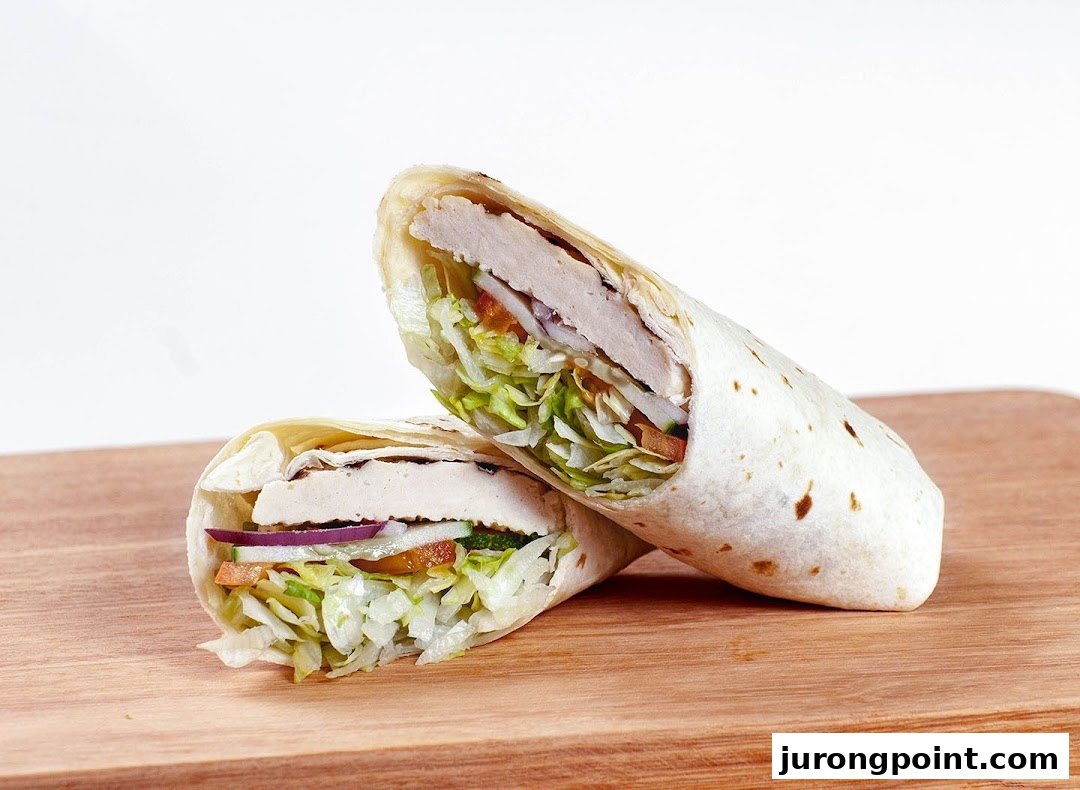 Two halves of a fresh chicken and vegetable wrap on a wooden board.