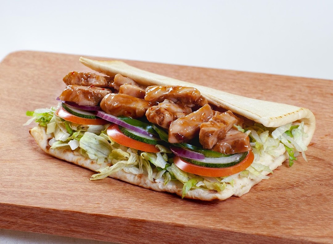 A delicious Subway flatbread sandwich filled with chicken, fresh vegetables, and sauce on a wooden board.
