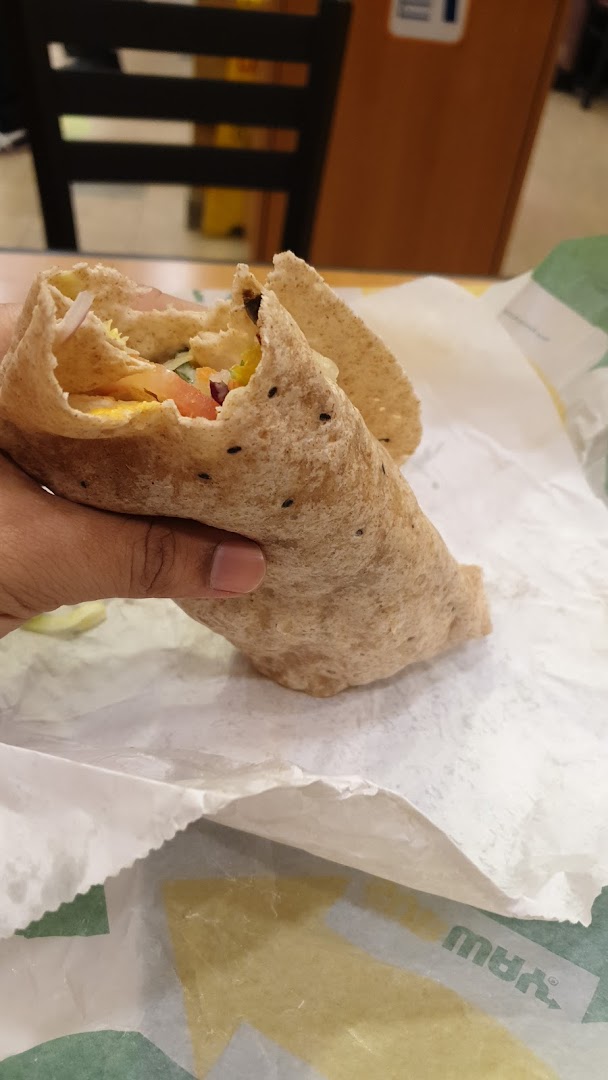 A hand holds a fresh Subway wrap, showcasing its wholesome ingredients on branded paper.