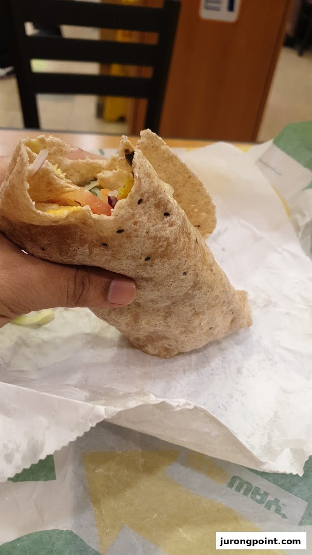 A hand holds a fresh Subway wrap, showcasing its wholesome ingredients on branded paper.