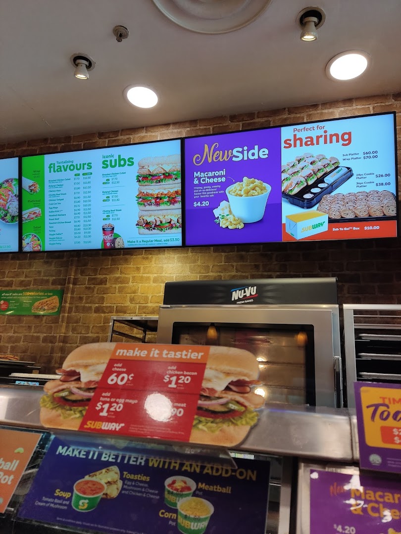 An interior shot of Subway showcasing their digital menu boards with various subs, sides, and platters.