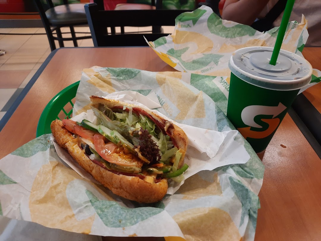 A fresh Subway sandwich in a basket with a branded drink on a table.