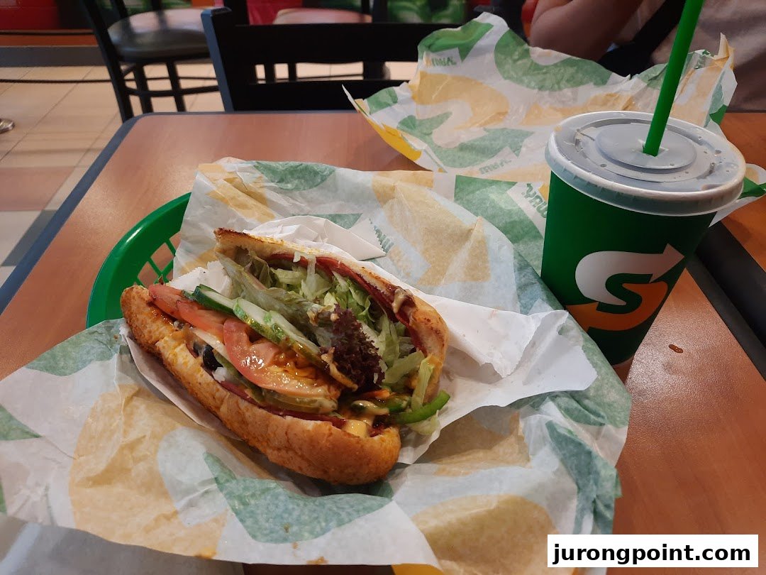 A fresh Subway sandwich in a basket with a branded drink on a table.