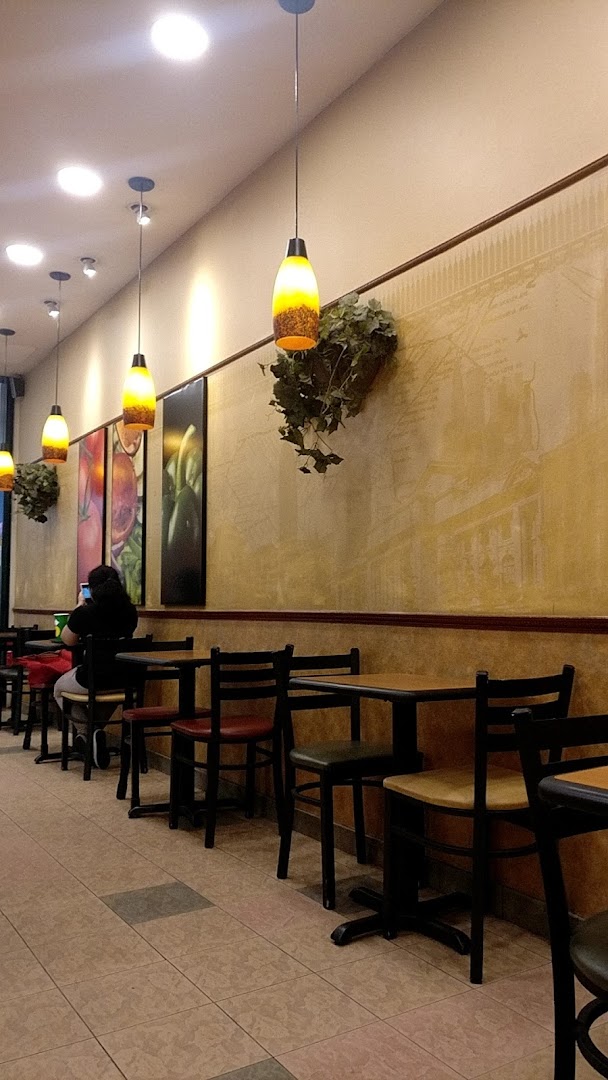 Interior view of a Subway restaurant with seating, tables, and decorative lighting.