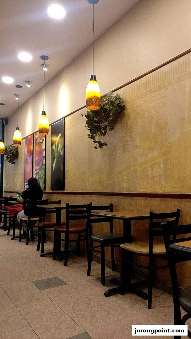 Interior view of a Subway restaurant with seating, tables, and decorative lighting.