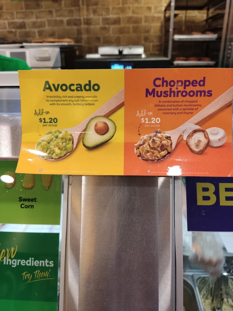 Close-up of Subway's add-on menu featuring avocado and chopped mushrooms with prices.