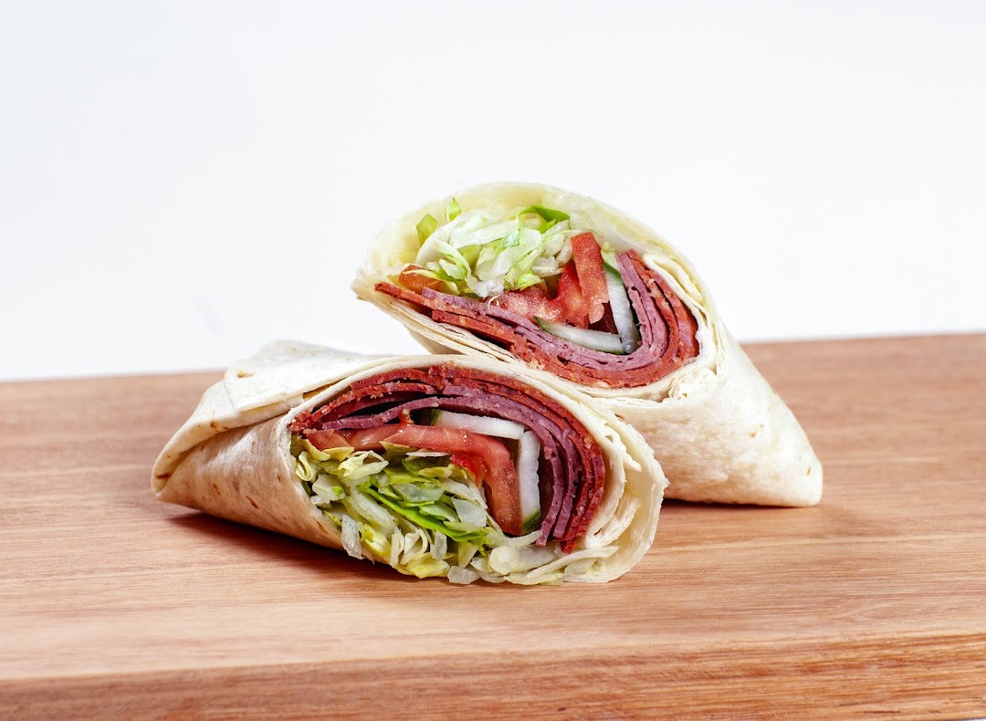 Two delicious wraps filled with sliced meat, fresh lettuce, tomatoes, and onions on a wooden board.
