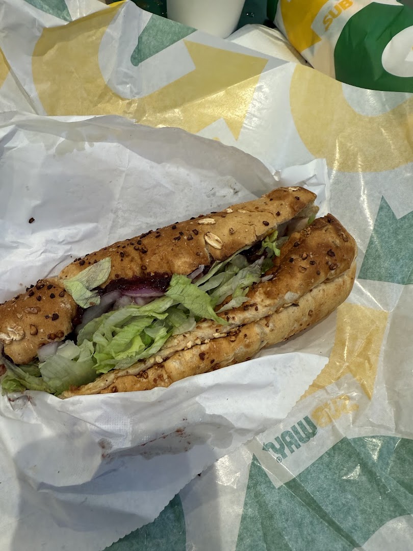 A freshly made Subway sandwich with lettuce and other fillings, wrapped in branded paper.