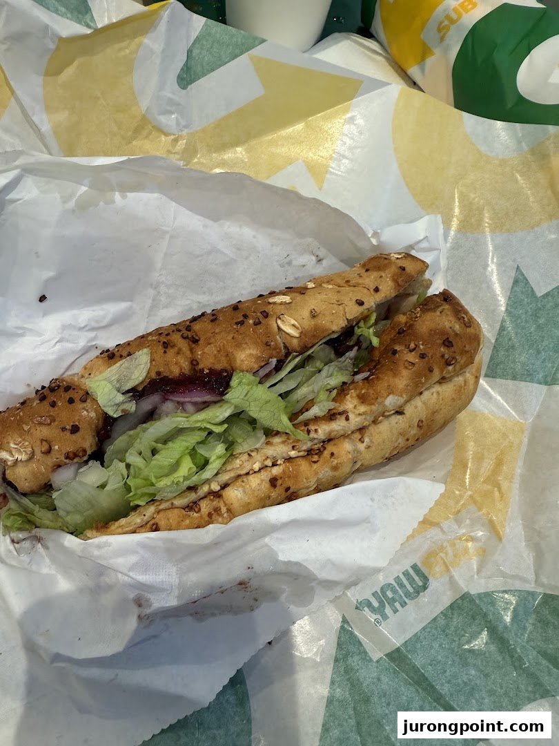 A freshly made Subway sandwich with lettuce and other fillings, wrapped in branded paper.