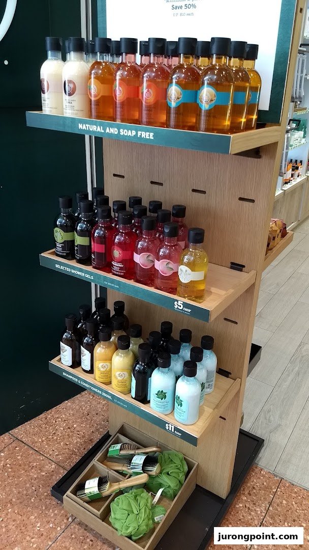 A display stand showcasing various Body Shop shower gels, shampoos, and bath accessories.